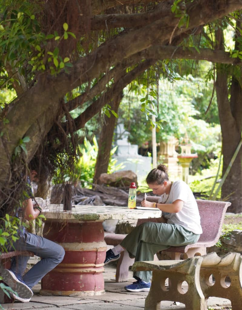 person journaling at stone table under tree