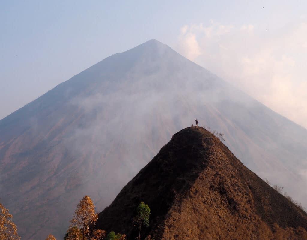 person silhouette at top of mountain look at another mountain