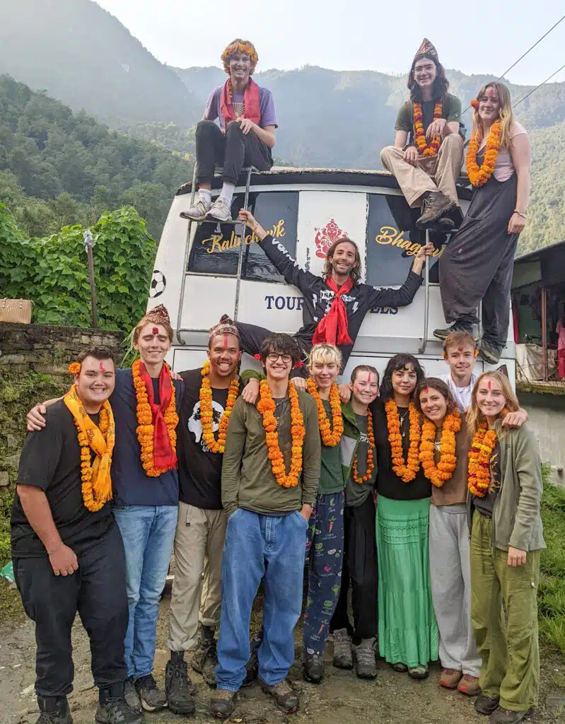 group smiling in front of van wearing marigold necklaces