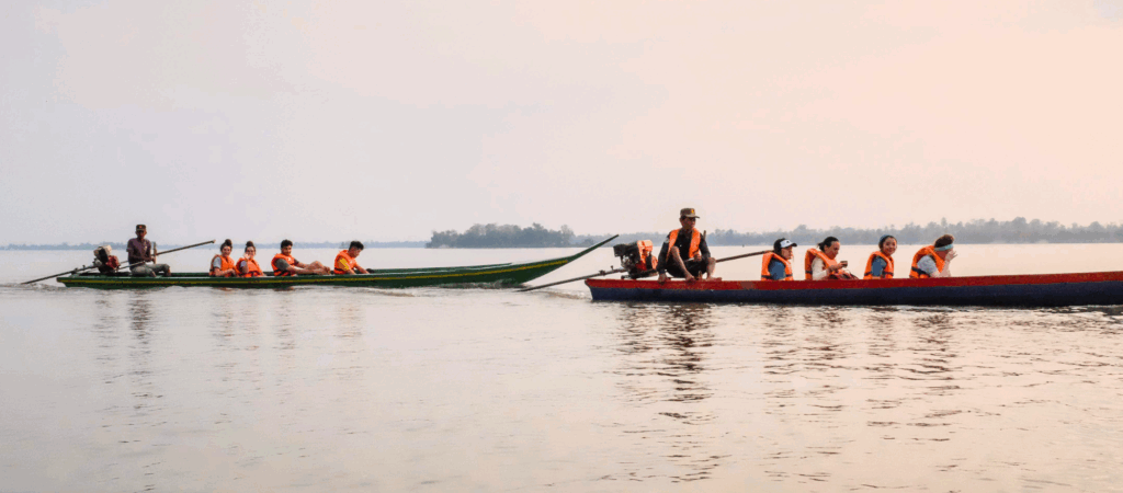 two long canoe boats with people in orange life jackets