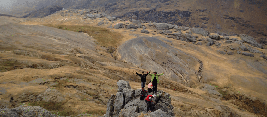 people standing on rock putting hands out to the sides with rocky and field backdrop